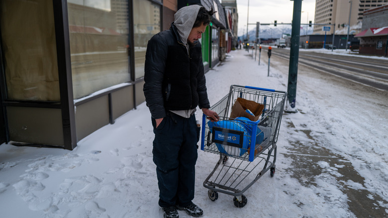 Man stands outside Anchorage Alaska shop holding cart on snowy street