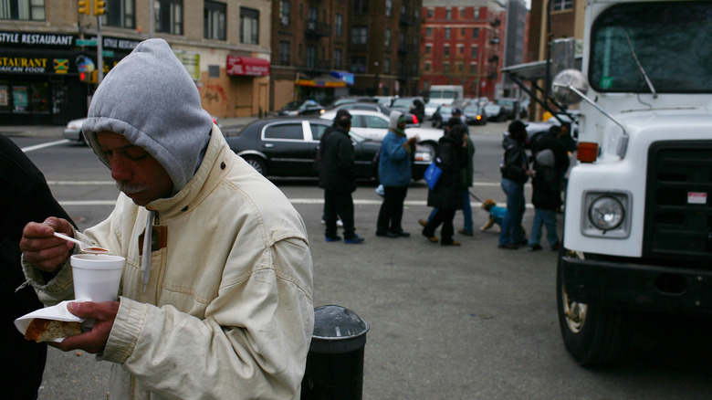 Man wearing hoodie eating soup out of cup in front of bus