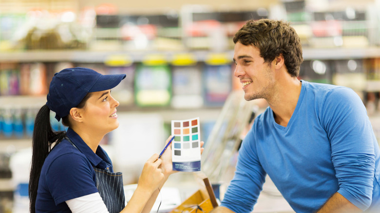 An employee at a paint store helps a man pick out the right color