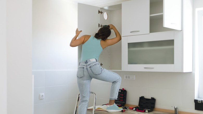 A young woman paints her kitchen cabinet white