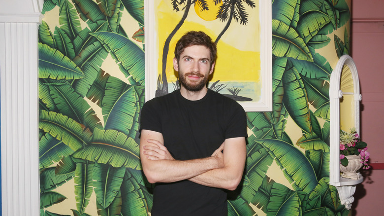 David Karp standing with his arms folded in front of a mural of tropical leaves.