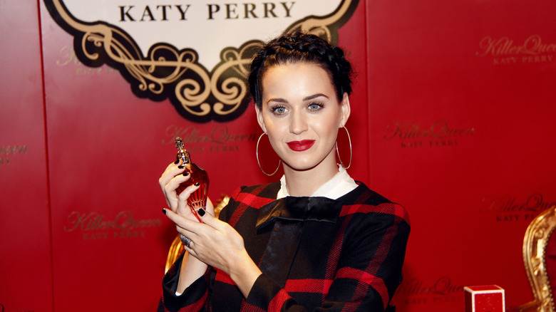 Katy Perry smiling while holding up a bottle of her fragrance Killer Queen.