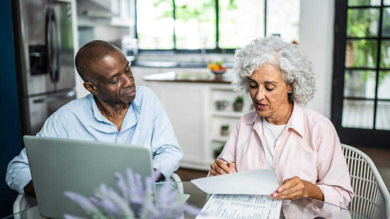 Two people looking at documents and a laptop while seated at kitchen table.