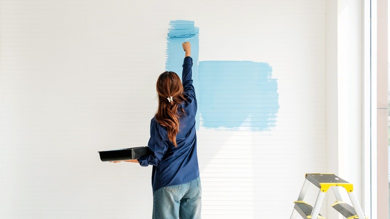 rear view of a woman painting the white wall of a room with light blue paint
