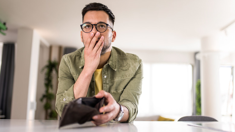 A concerned man holding an empty wallet