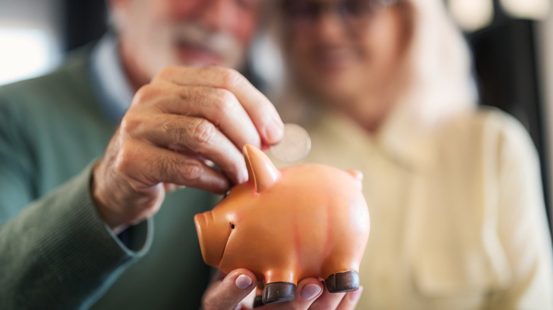 Mature couple placing money into a piggy jar.