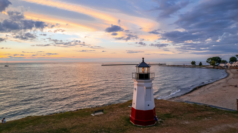 A small white and red lighthouse on the coast, with water beyond it.