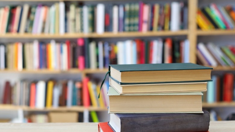 A stack of books in front of shelves of books.