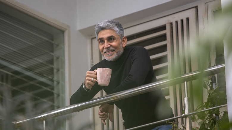 A smiling mature man enjoying a cup of coffee on a balcony.