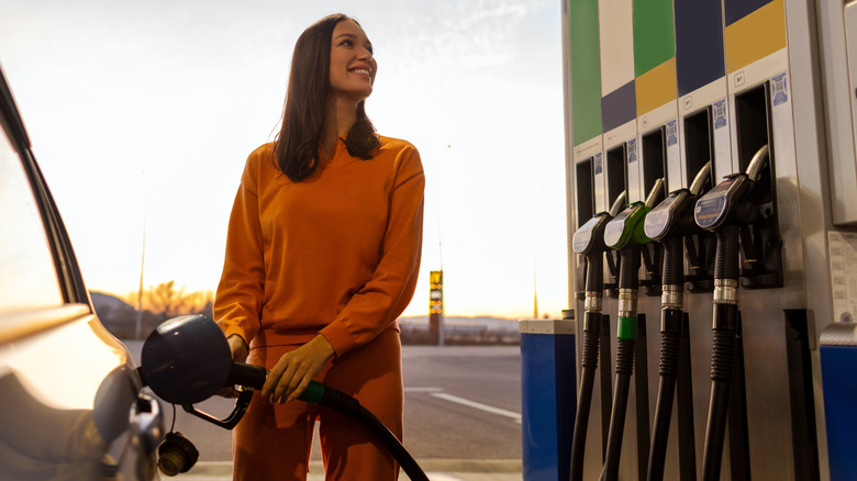A young woman smiles as she fills her car up with gas