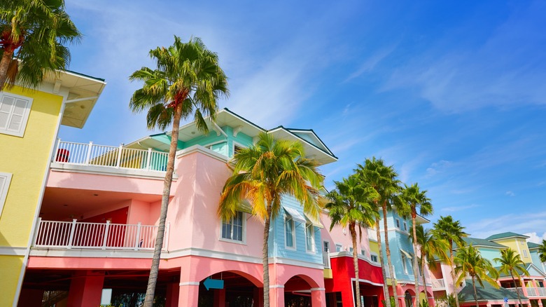 Colorful pastel waterfront homes in Fort Myers with balconies, palm trees, and a bright blue sky, giving the scene a tropical coastal feel