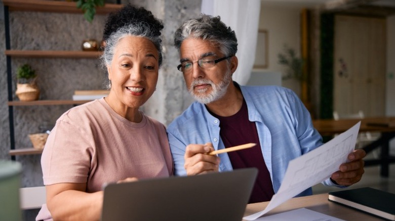 An middle-aged couple planning for retirement looking at papers and a laptop in their home.
