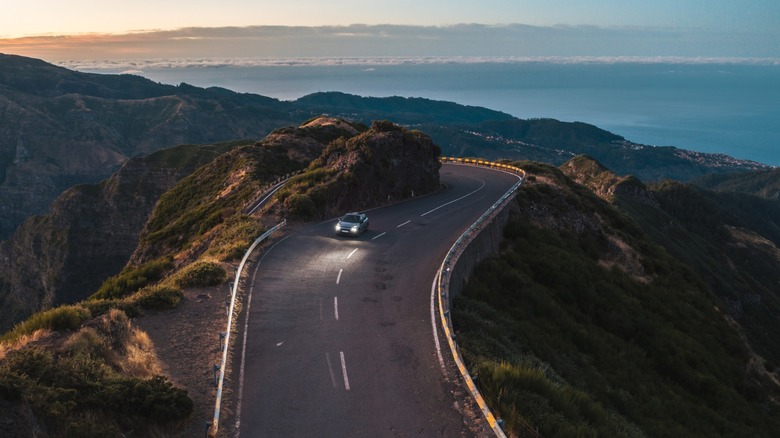 Lone car at sunset driving on a winding, hilly road
