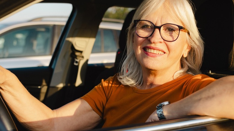 A senior woman smiling while placing her hands on the steering