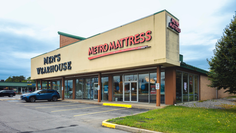 A Metro Mattress location in a strip mall next to a Men's Wearhouse on a lightly cloudy day