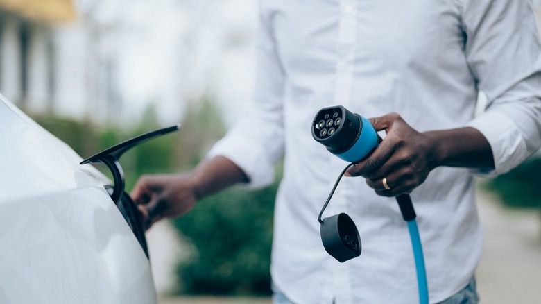 Person holding an EV charging cable beside a white electric car