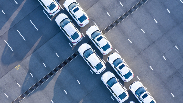A striking image of white sedans and SUVS in a two car row on empty parking lot, in an aerial image