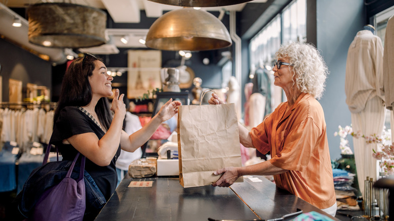 A mature saleswoman handing a shopping bag to a smiling Gen Z woman.
