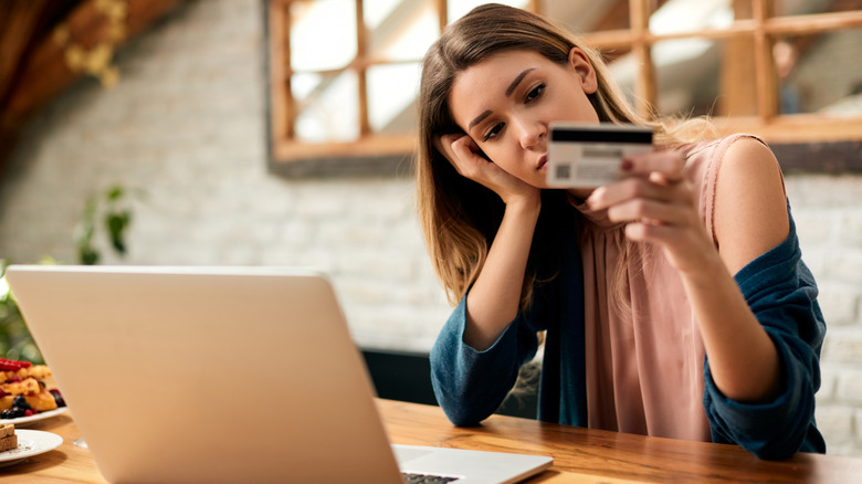 A young woman depressed over mounting bills staring at her credit card