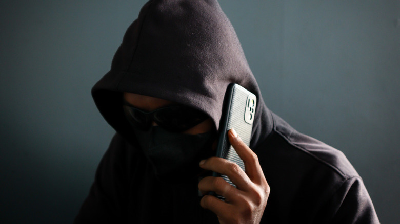 a scammer holding phone with hood up