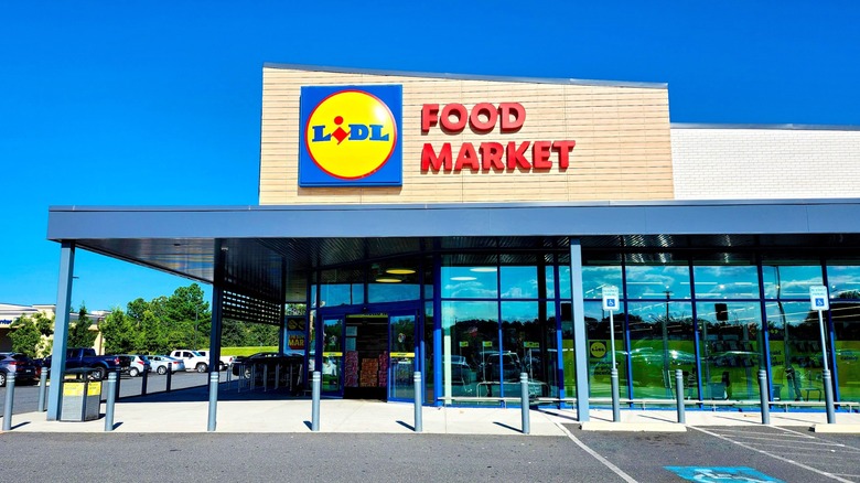 Exterior of a Lidl Food Market with a glass storefront and accessible parking spaces under a clear blue sky