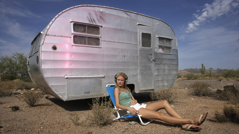 A young woman lounging outside of a mobile home in the desert
