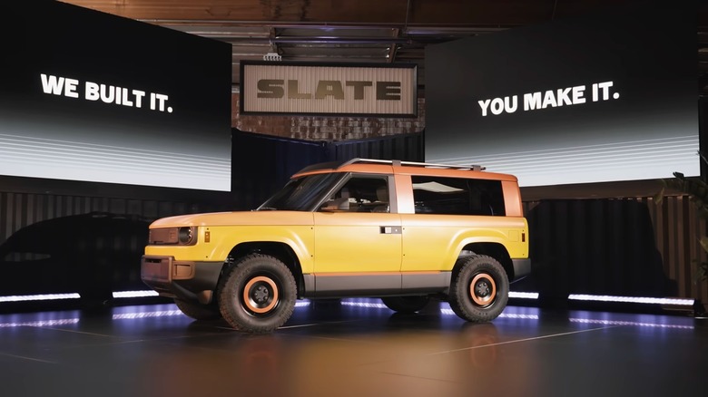 A yellow-and-orange Slate SUV conversion displayed onstage beneath the Slate logo, with screens reading, "We built it. You make it."