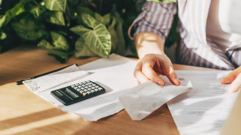 woman checking receipts and calculating bills next to a plant