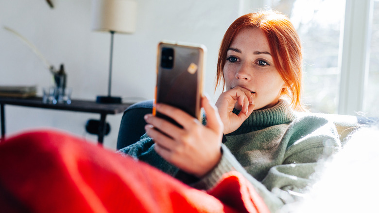 Woman with red hair looking on screen of her mobile phone.