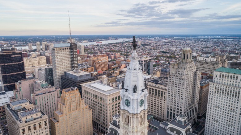 The top of Philadelphia's city hall with its statue of William Penn surrounded by tall buildings in the center city area.
