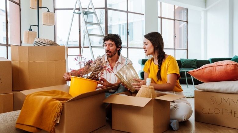 A young couple sitting on the floor while unpacking moving boxes inside of a new home.