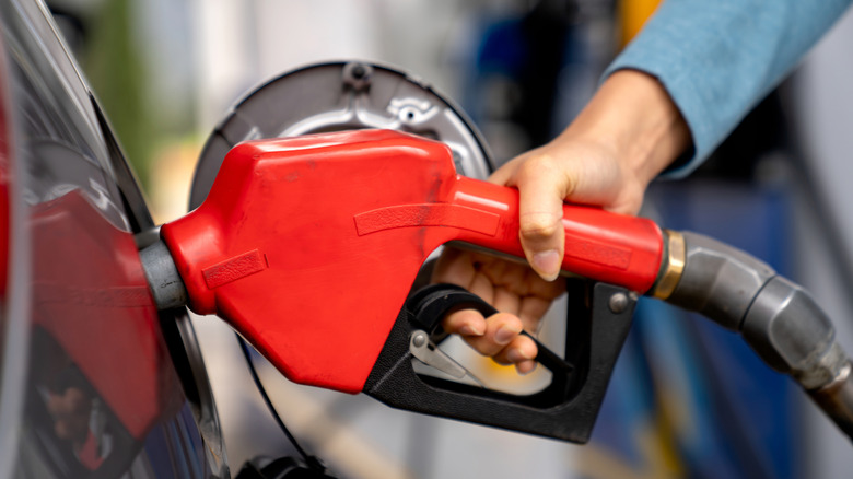 A person placing a gas pump nozzle inside a car's open fuel filler.