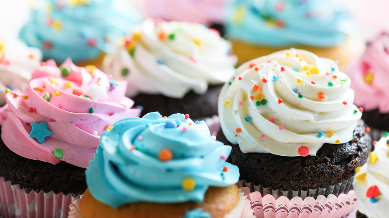 Several cupcakes with blue, white, and pink frosting and sprinkles on top.