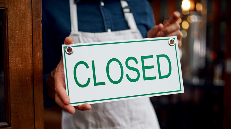 closed sign pressed against window by man with apron.