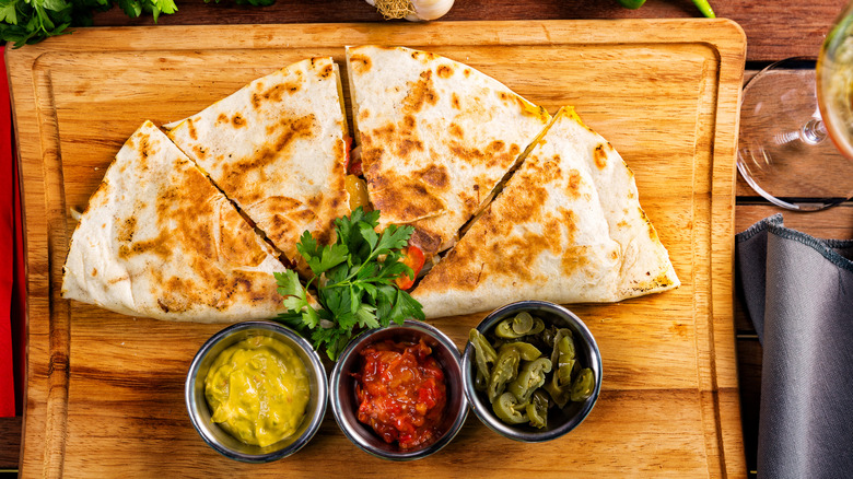 Four quesadillas with three different sauces on cutting board