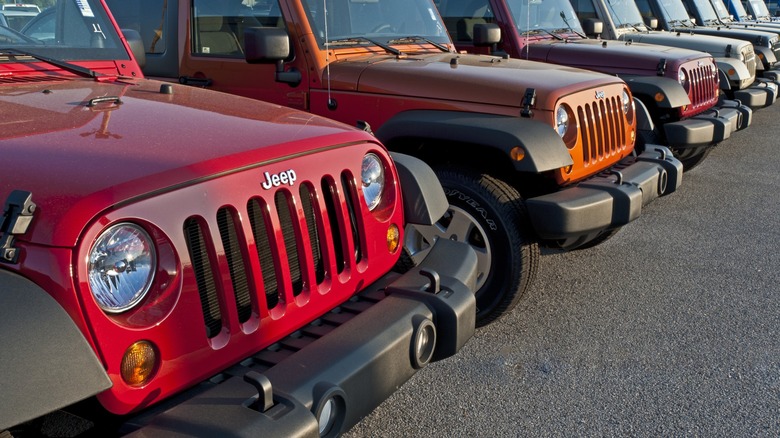 Red, orange, burgundy, and silver Jeep Wranglers lined up in a dealership lot