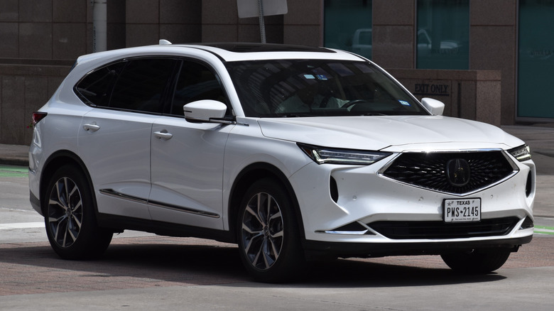 Beige Acura MDX interior with leather seats, wood trim, center console controls, and dashboard display shown from the front passenger side