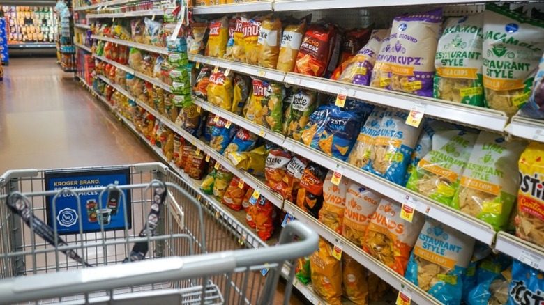 An empty shopping cart in the chip aisle of a Kroger grocery store.