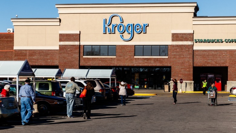 A Kroger grocery store exterior with a large parking lot in front of it filled with cars and shoppers.