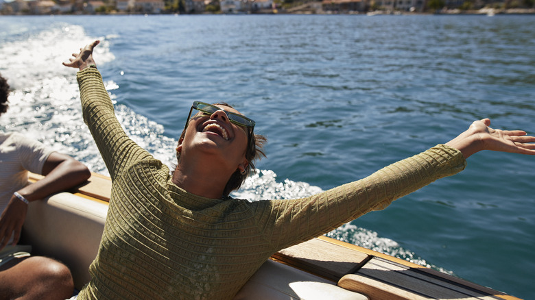 Happy young woman with arms raised in motorboat enjoying sunny day