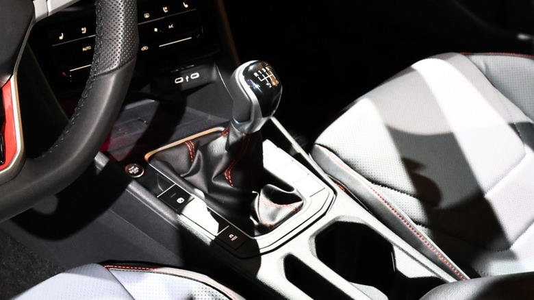 Close-up of the 2026 Volkswagen Jetta GLI's interior showing the six-speed manual gear shifter, center console, cupholders, and front seats with red stitching