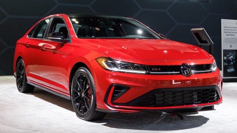 Front three-quarter view of a red Volkswagen Jetta GLI on display at an auto show, featuring black alloy wheels, LED headlights, and GLI badging against a dark backdrop