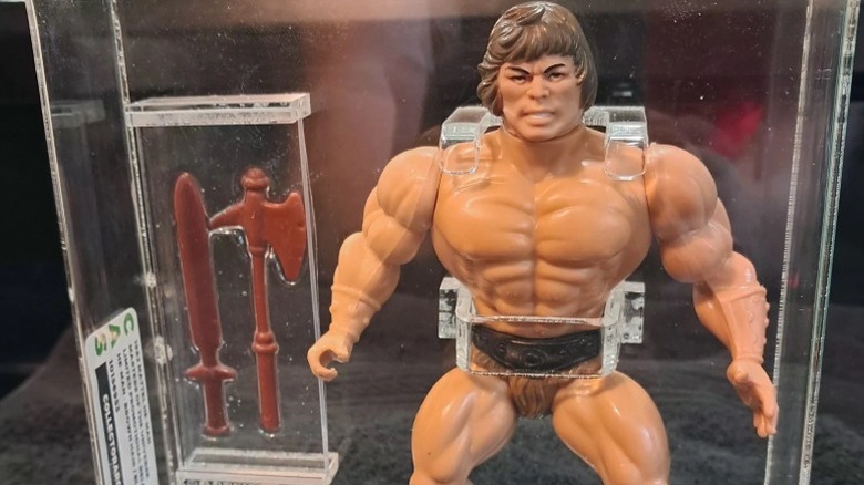 A Wonder Bread Savage Wun-Dar He-Man action figure toy in a glass display case with two plastic weapons.