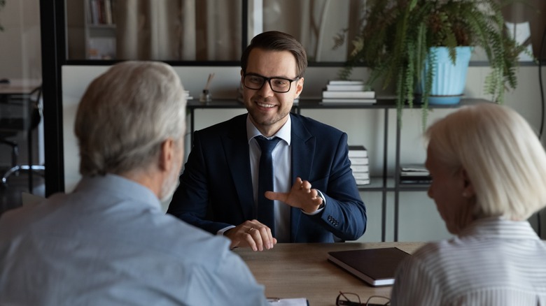 Man speaking with an older couple across a desk in an office