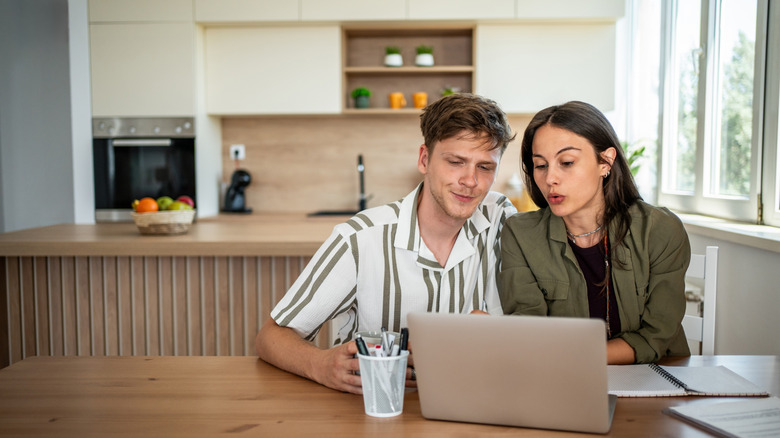 A young couple looking at a laptop white sitting at a table.