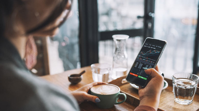 Woman checking investment charts on her smartphone while at a coffee shop.
