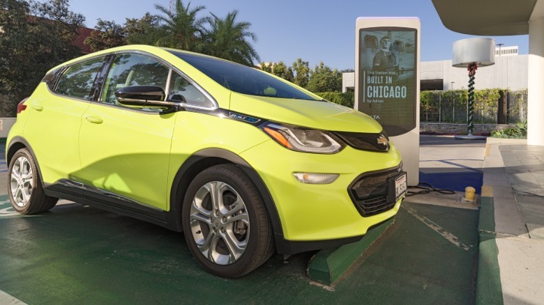 A lime green used Chevrolet Bolt EV at a charging station in a parking lot on a sunny day.