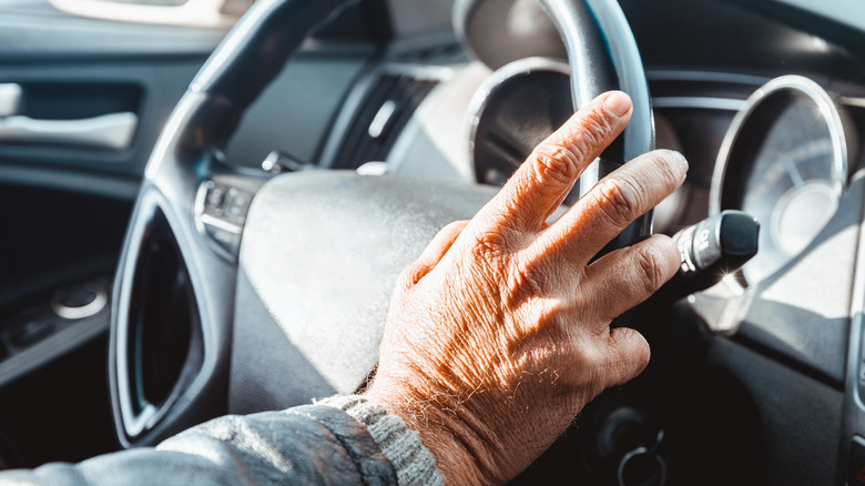 A mature hand on a car steering wheel.