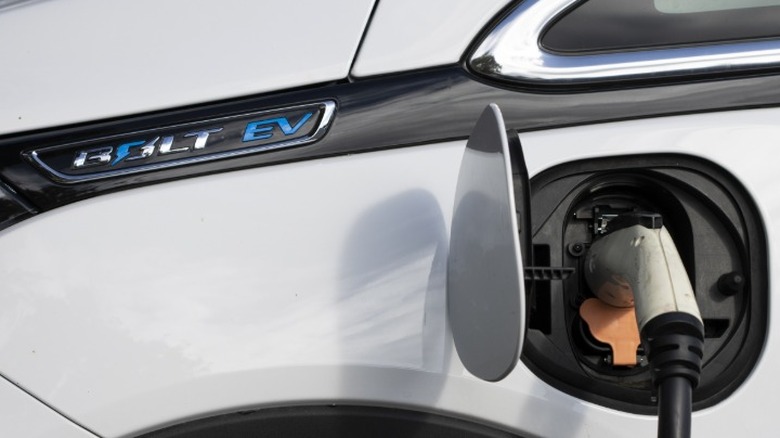 The charging port with a charger plugged in on a white Chevy Bolt EV vehicle.