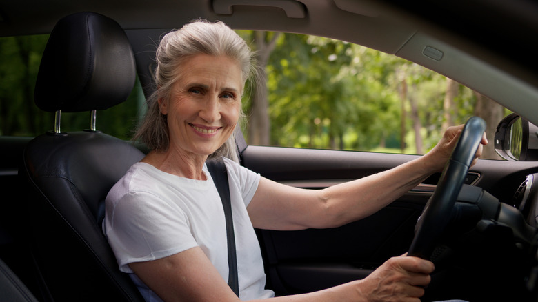 A woman retiree sitting in a car smiling.